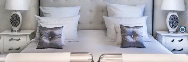 Elegantes Doppelbett mit aufgeschütteten Kissen und Decke in einem modern eingerichteten Schlafzimmer. Symbol für Komfort und erholsamen Schlaf.